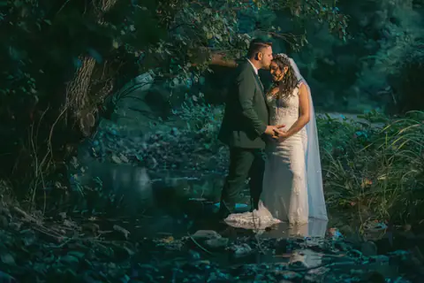 Los novios abrazados junto al agua, a la sombra de un árbol