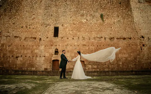 Los novios ante una muralla de piedra, con el velo extendido por el viento